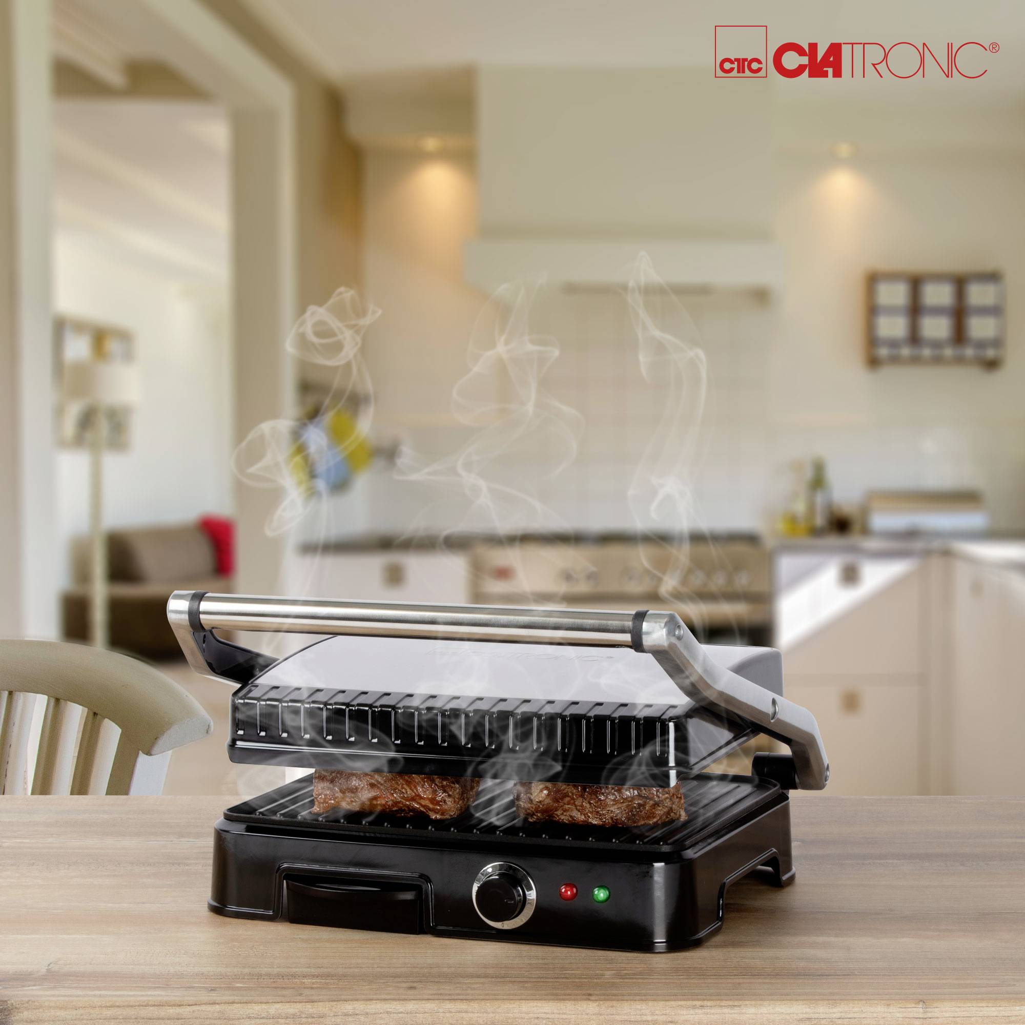Elektrische grill in een keuken; stoomende steaks worden gegrild. Op de achtergrond is een lichte, moderne keuken te zien.
