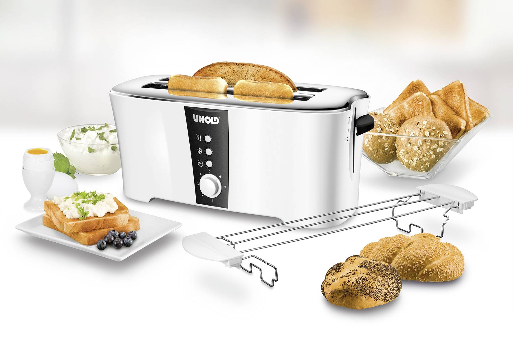 Een witte broodrooster met twee toastplakken, omringd door brood, broodjes en ontbijttoebehoren zoals eieren en yoghurt.