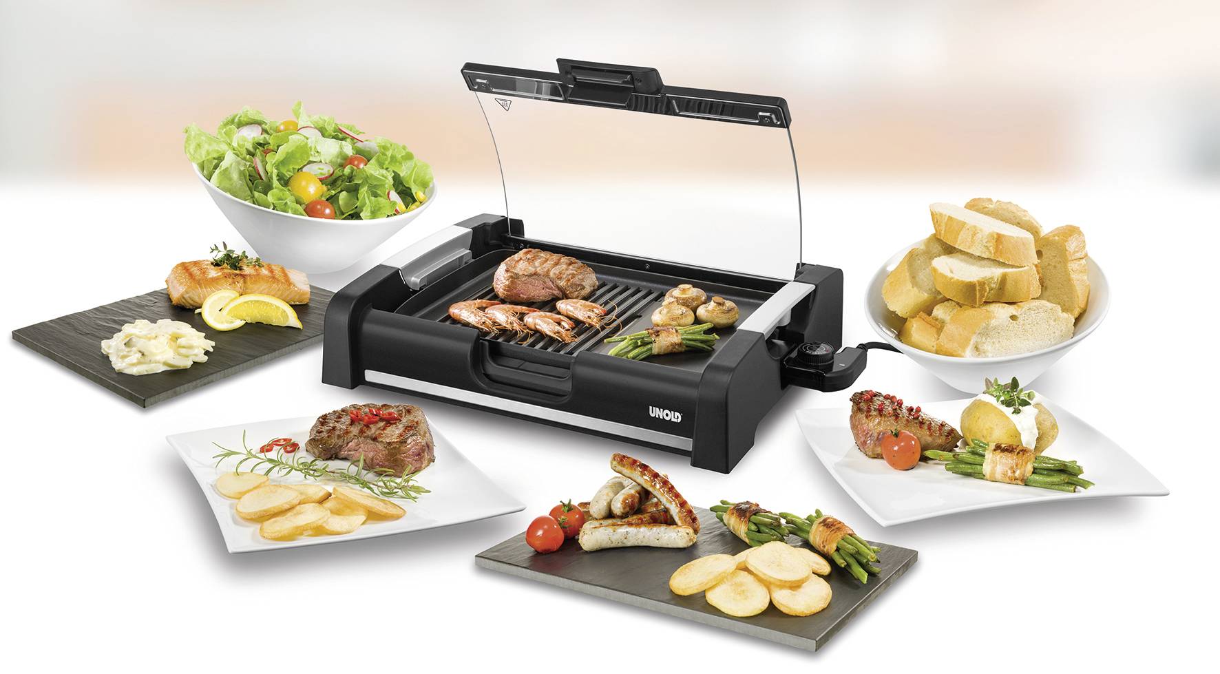 Een tafelgrill met gegrild vlees, worstjes en groenten. Ernaast borden met brood, salade, aardappels en garnalen.