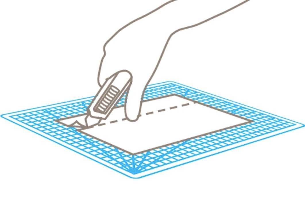 Een hand snijdt langs een stippellijn op papier dat op een snijmat ligt, met een scherp mes.