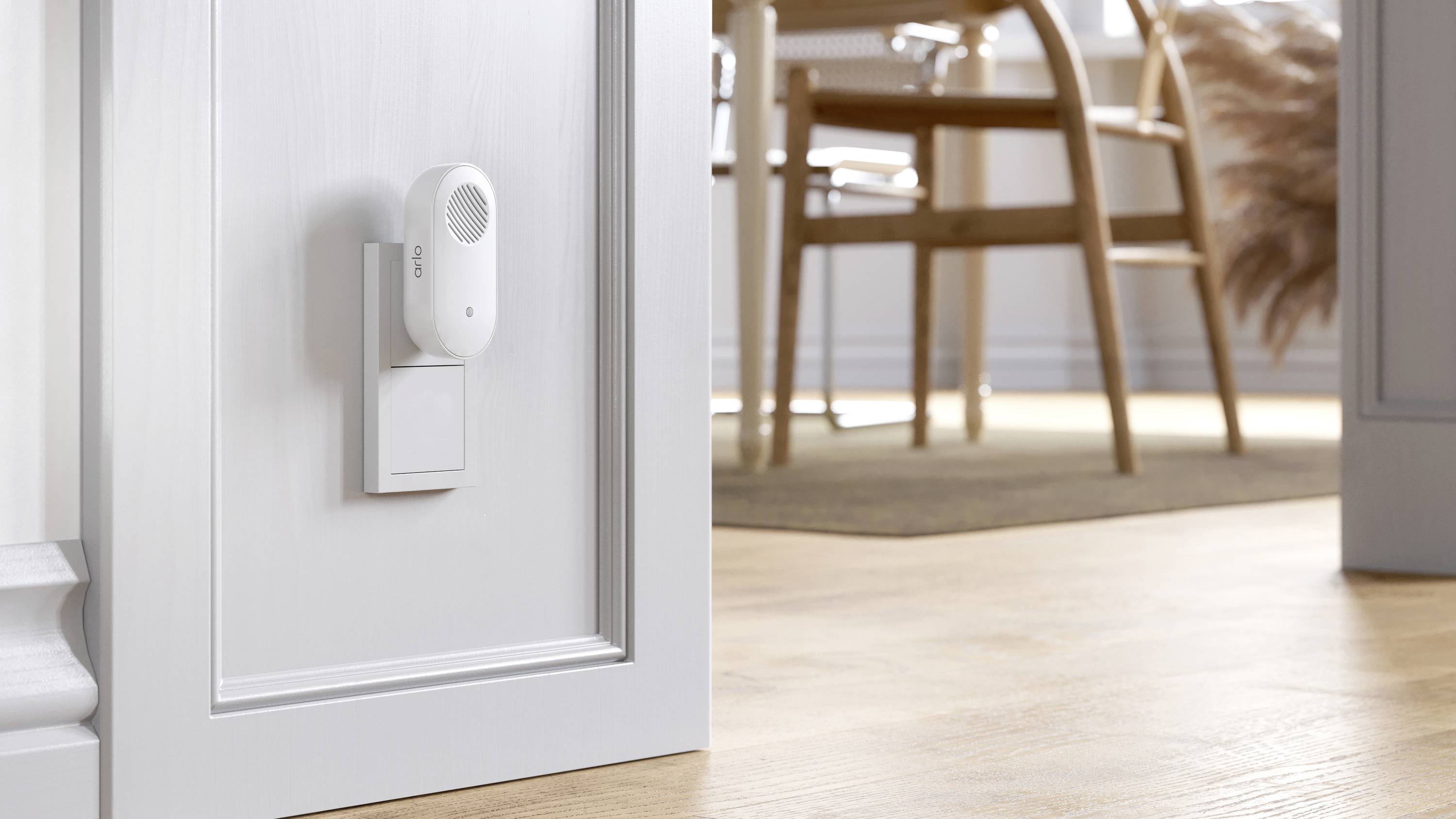 Een kleine, witte luchtreiniger steekt in een stopcontact in een lichte ruimte. Op de achtergrond zijn een tafel en stoelen zichtbaar.