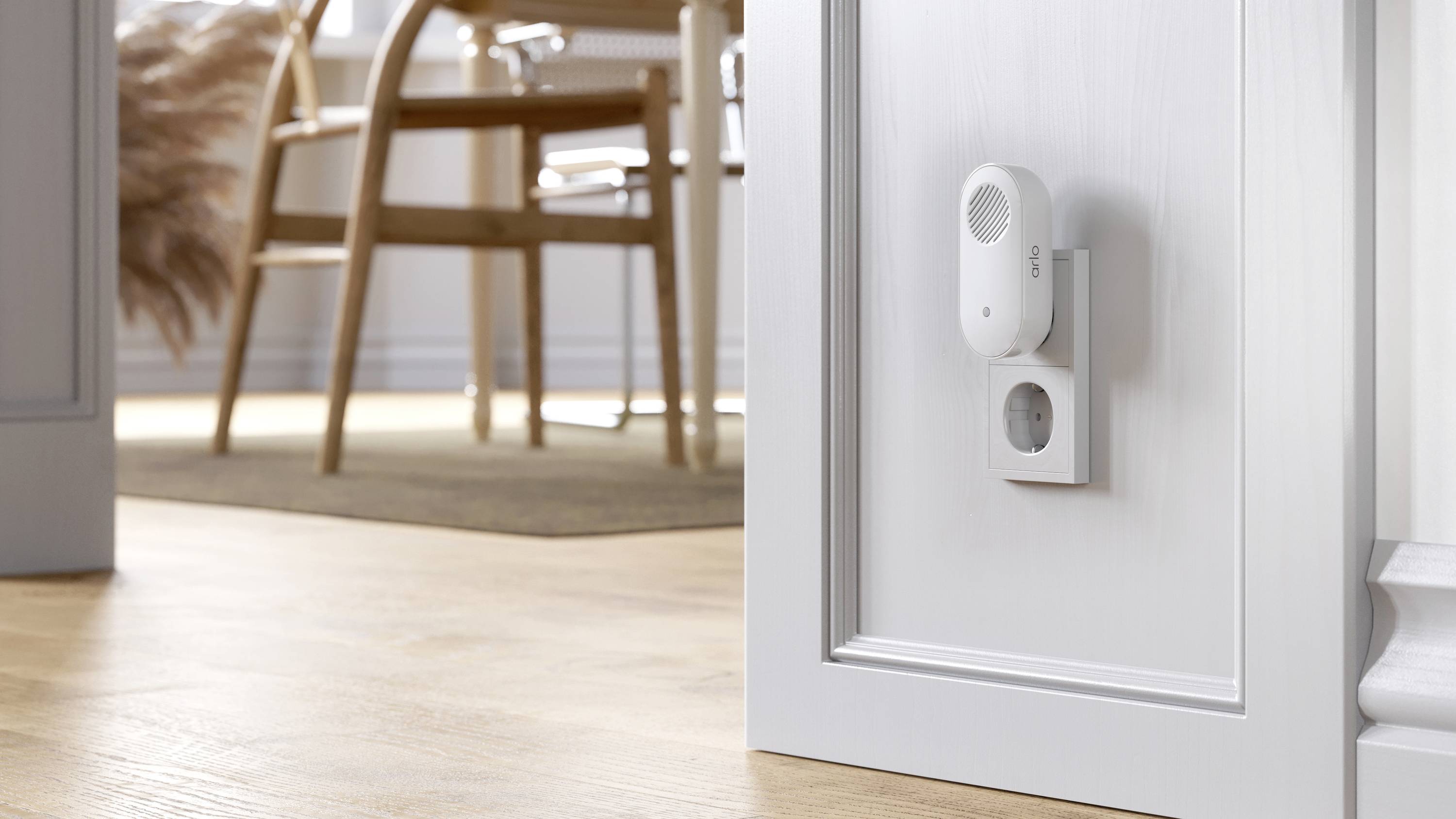 Een witte deurcontactsensor is bevestigd in het onderste deel van een deurkozijn. Op de achtergrond zijn delen van een eetkamer zichtbaar.