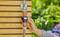 Een persoon stelt een digitale watertimer in die aan een waterslang is bevestigd aan een houten muur, met een tuin op de achtergrond, wat wijst op gebruik buitenshuis.