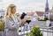 Een vrouw met lichte haren staat op een balkon en stelt een meteorologisch instrument af. Op de achtergrond zijn stadshuizen zichtbaar.
