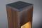 Houten zuil met geïntegreerde verlichting die een warme gele gloed produceert, tegen een grijze achtergrond. Minimalistisch en modern design.