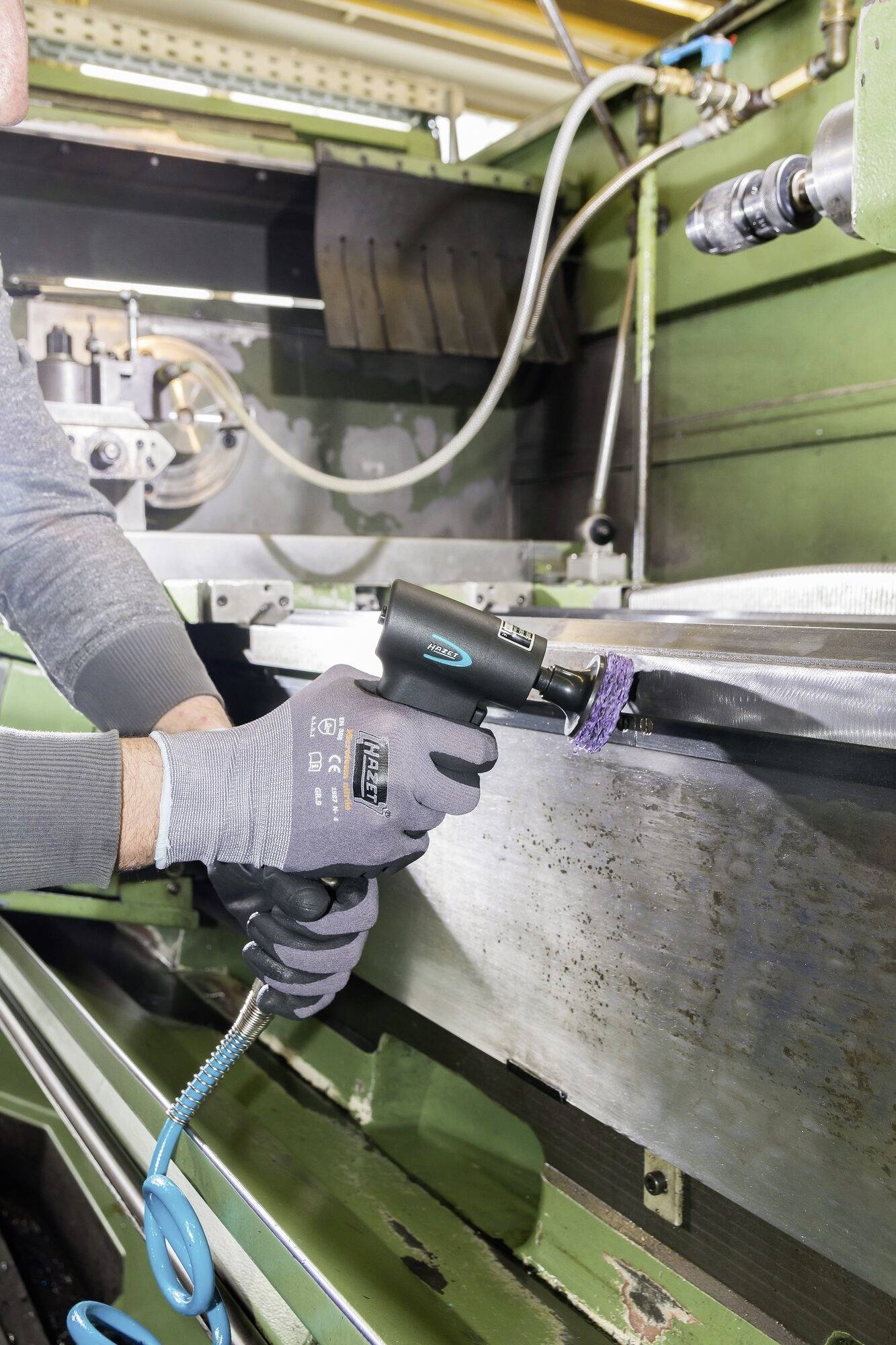 Een persoon draagt handschoenen en gebruikt een elektrisch gereedschap om metaal te slijpen in een werkplaatsomgeving.