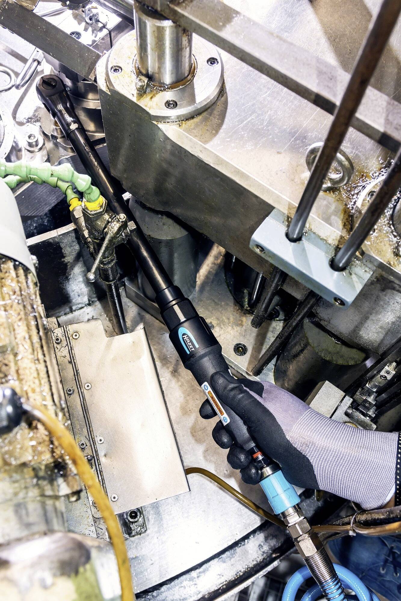 Een arbeider gebruikt een handgereedschap in een industriële omgeving om een machine te repareren. Het gereedschap heeft een ergonomische handgreepvorm.