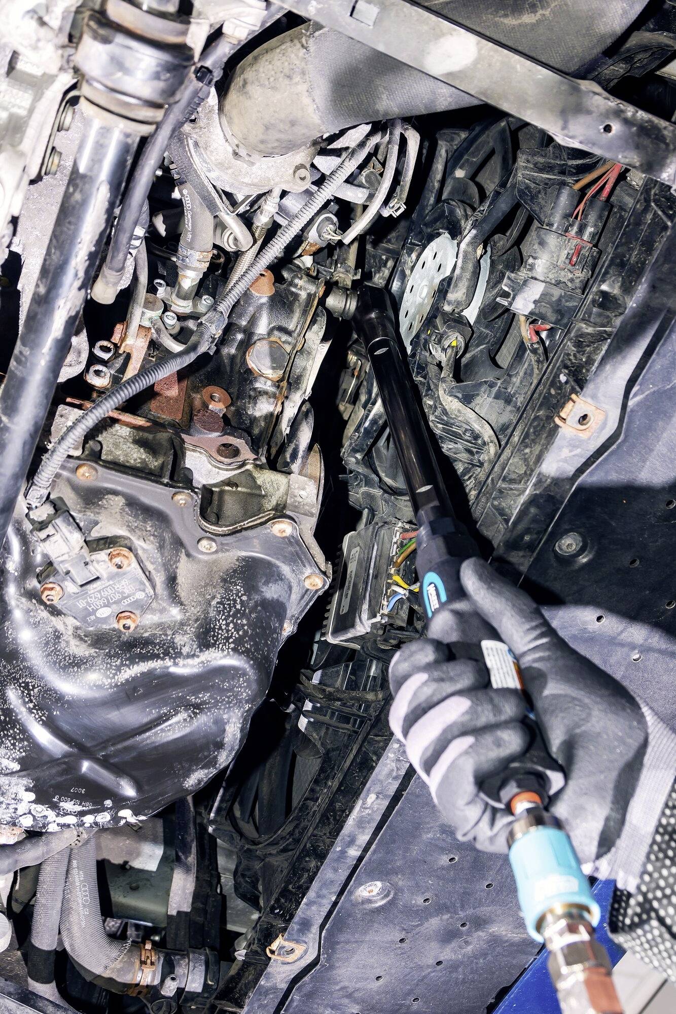 Een monteur repareert de motor van een auto in een werkplaats. De focus ligt op de kabels en aansluitingen in de motorruimte.