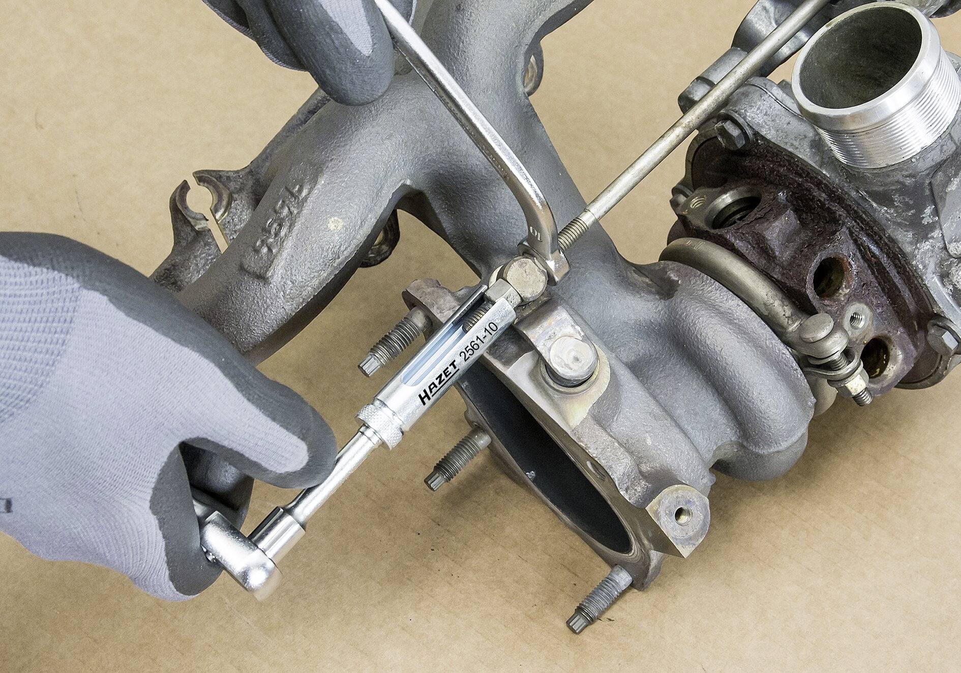 Een persoon met een grijze handschoen gebruikt een momentsleutel om een schroef aan een metalen autoonderdeel aan te draaien.