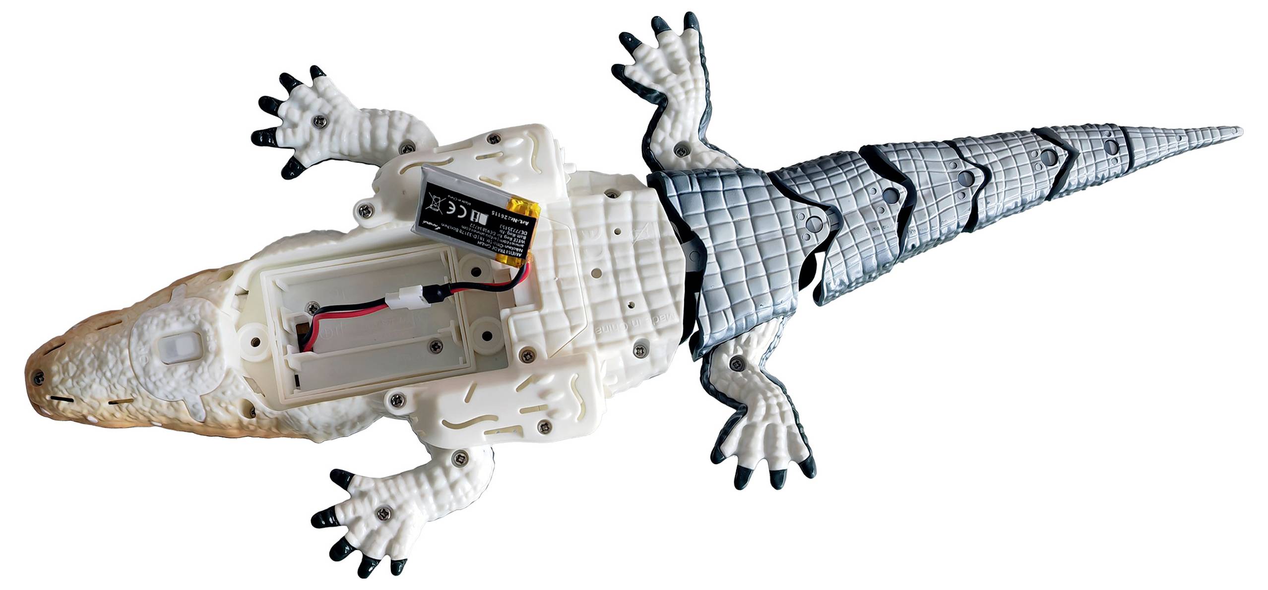 Opengescheurd speelgoed-krokodil toont interne elektronica en batterij; gezien van bovenaf.