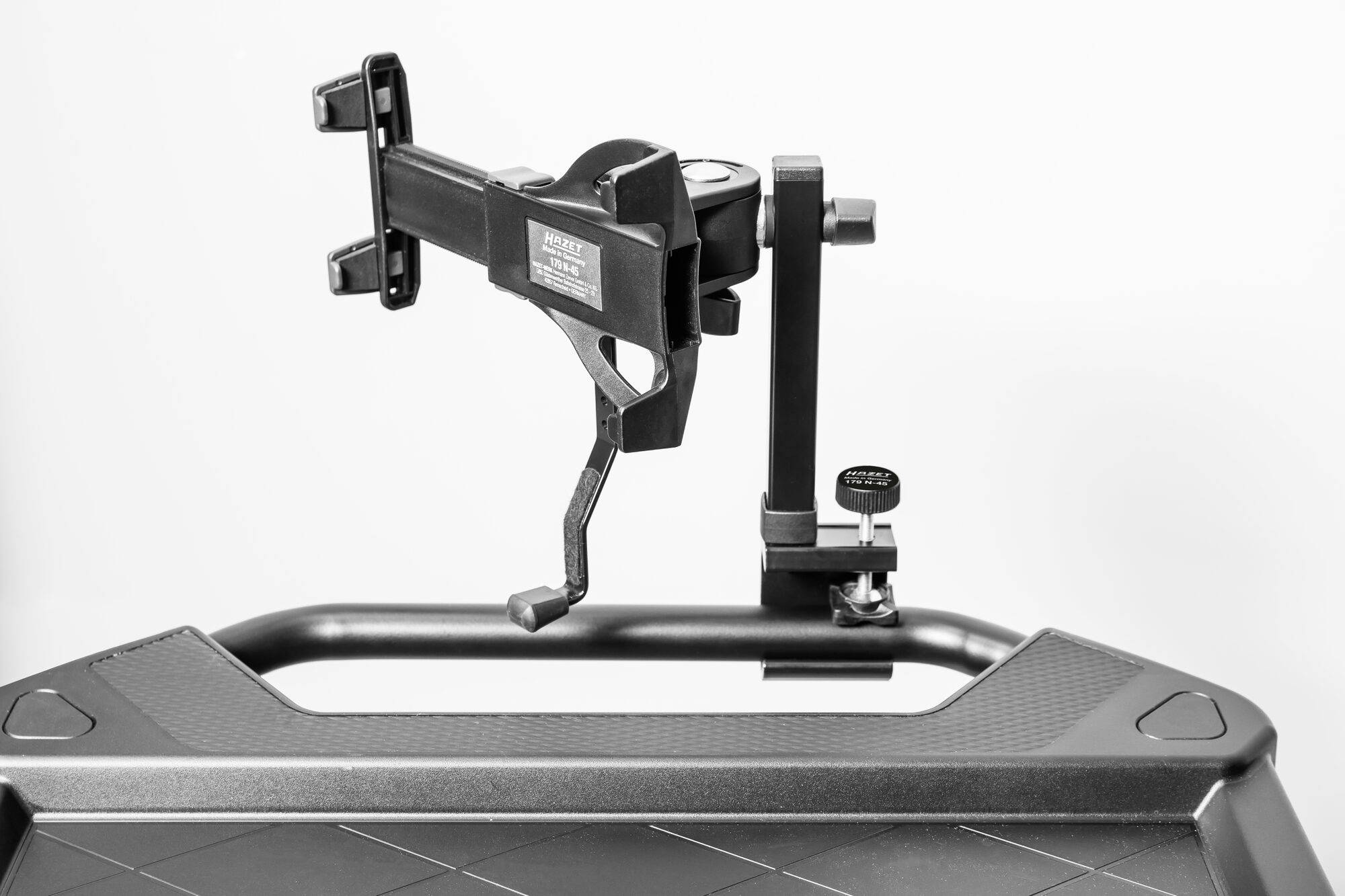 Een zwarte houder met klembevestiging is gemonteerd op een metalen frame. De houder heeft beweegbare onderdelen voor aanpassing.