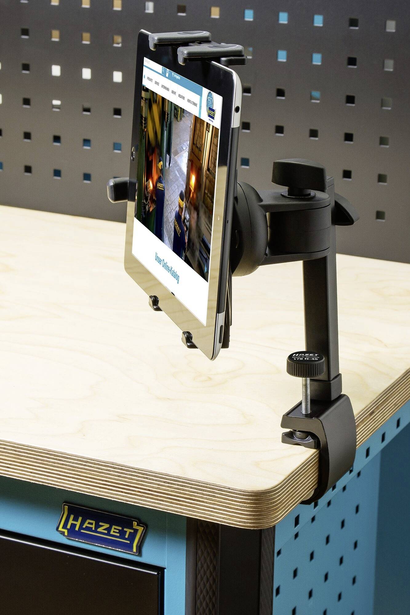 Een tablethouder is bevestigd aan een tafel. Er wordt een tablet getoond met een geopende webpagina. De omgeving oogt technisch modern.