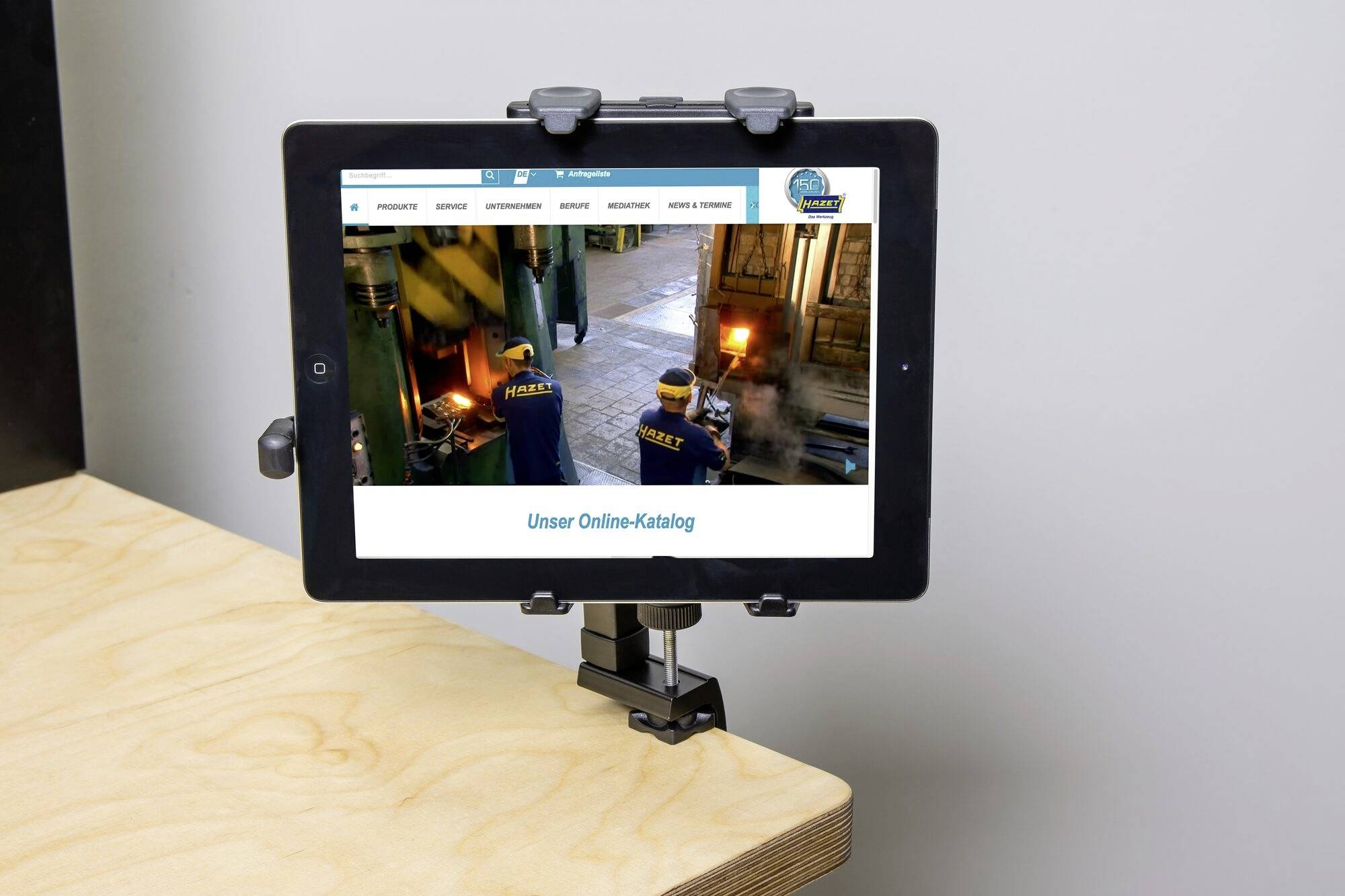Een tablet met een geopende webpagina toont 'Onze online catalogus'. Het is bevestigd in een houder op een tafel.
