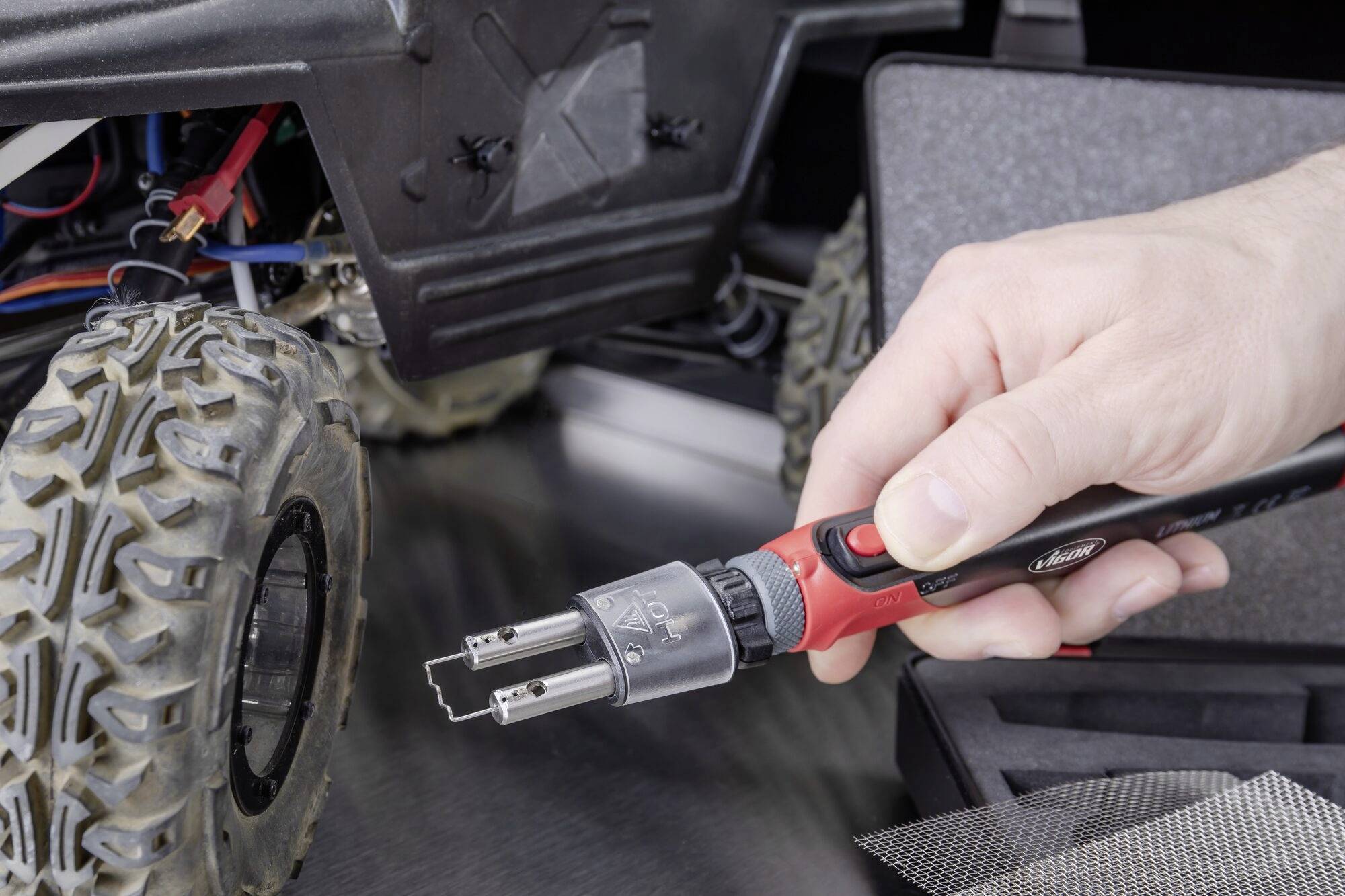 Close-up van een hand die met een multifunctioneel gereedschap werkt aan een modelvoertuigband. De focus ligt op het gebruik van het gereedschap.