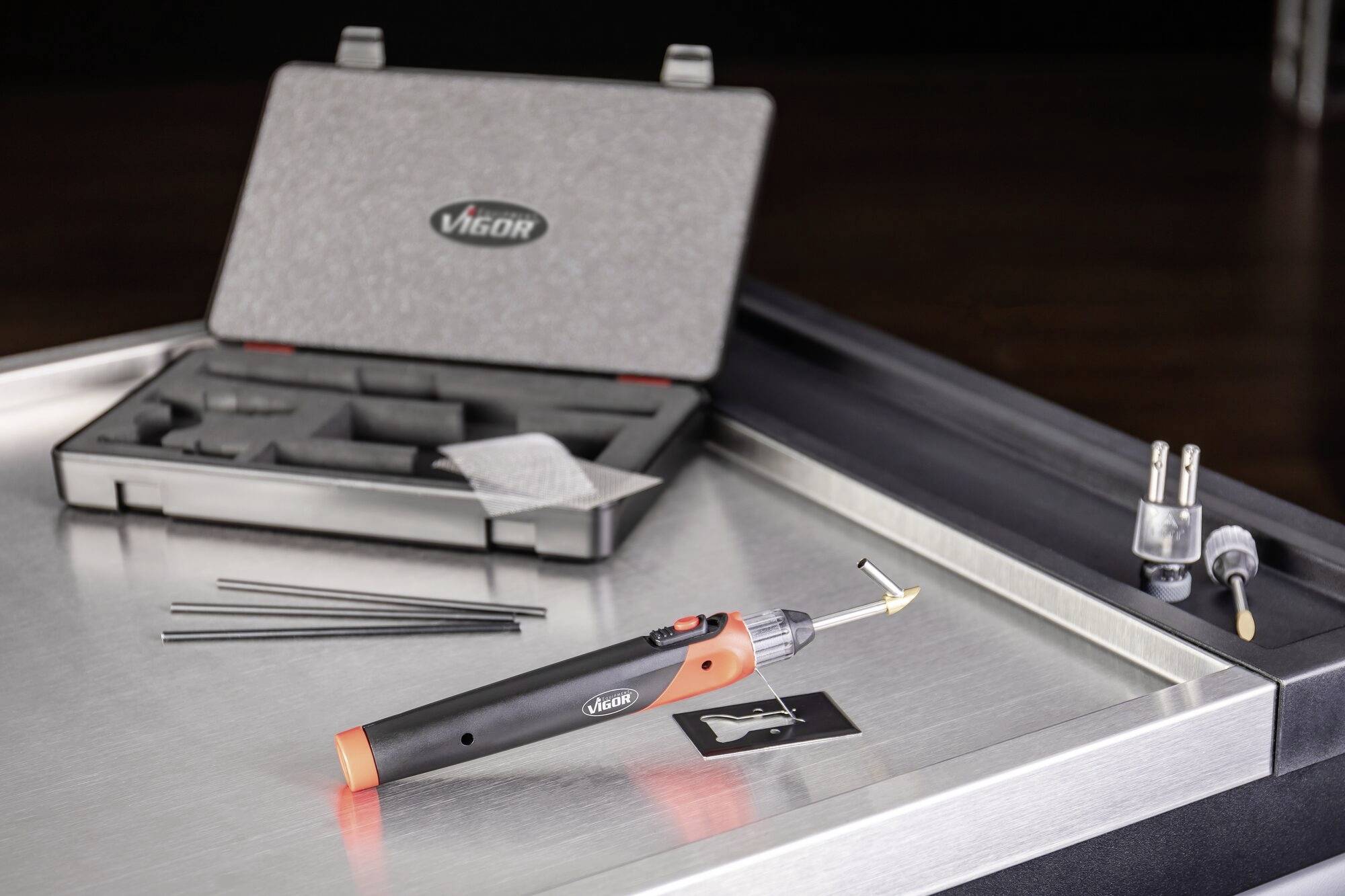 Soldeerboutset op een tafel met een open koffer op de achtergrond. Het set bevat een soldeerbout, soldeerstaafjes en een handleiding.