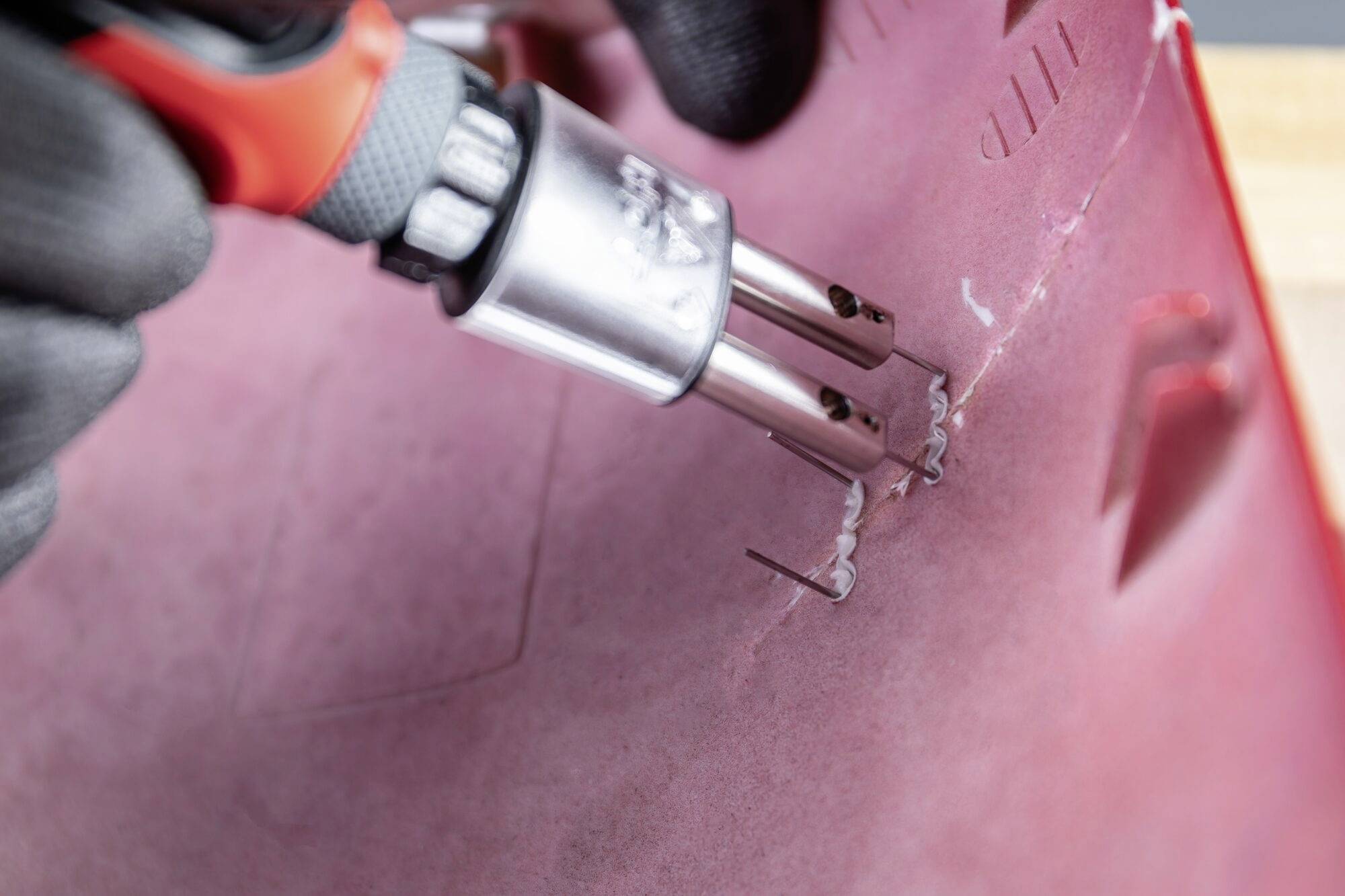 Een persoon repareert een rood kunststofvoorwerp met een soldeerbout om scheuren te dichten. De focus ligt op de reparatieplek.