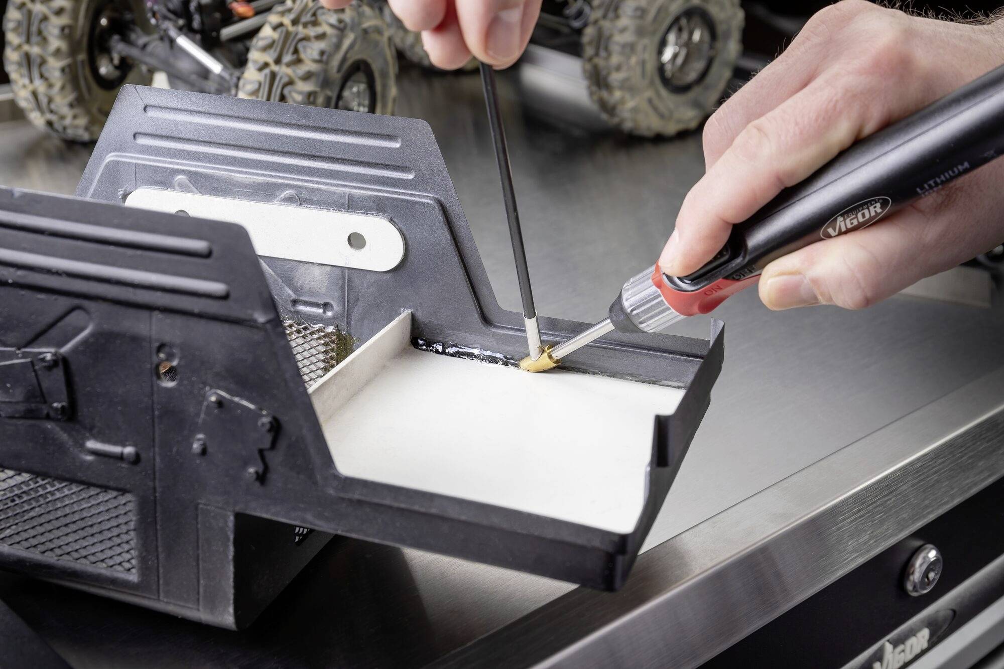 Een hand soldeert met een soldeerbout aan een modielauto. De focus ligt op precisiewerk aan de elektronica van het voertuig.