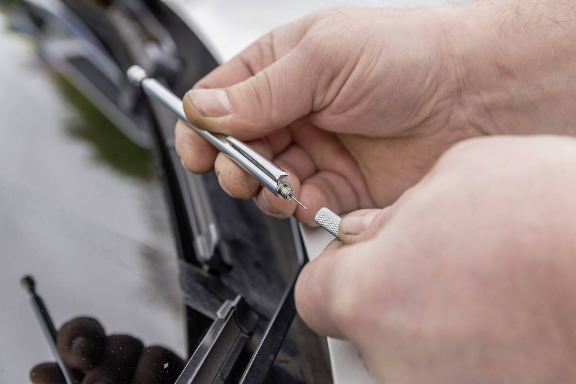 Close-up van een persoon die een klein gereedschap gebruikt om een steenslag in een autoruit te repareren.