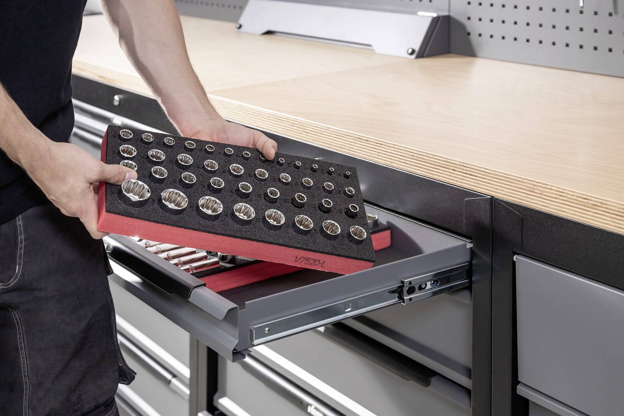 Een persoon plaatst een set steeksleutels in een lade van een werkbank. De werkbank heeft een houten oppervlak.