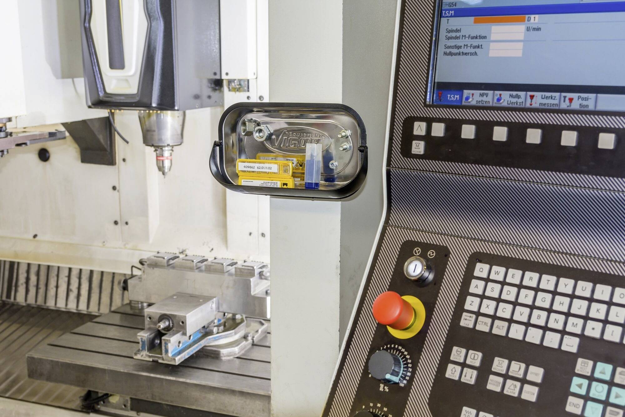 CNC-freesmachine met scherm toont bewerkingsproces. Bedieningspaneel met knoppen op de voorgrond, metalen blok op de frestafel.