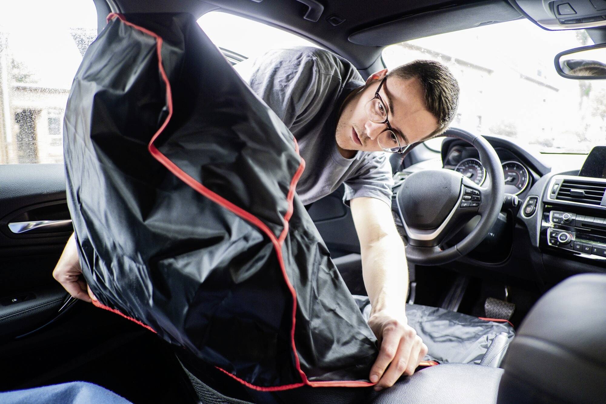 Een persoon reinigt het interieur van een auto met een zwarte afdekking met rode rand.