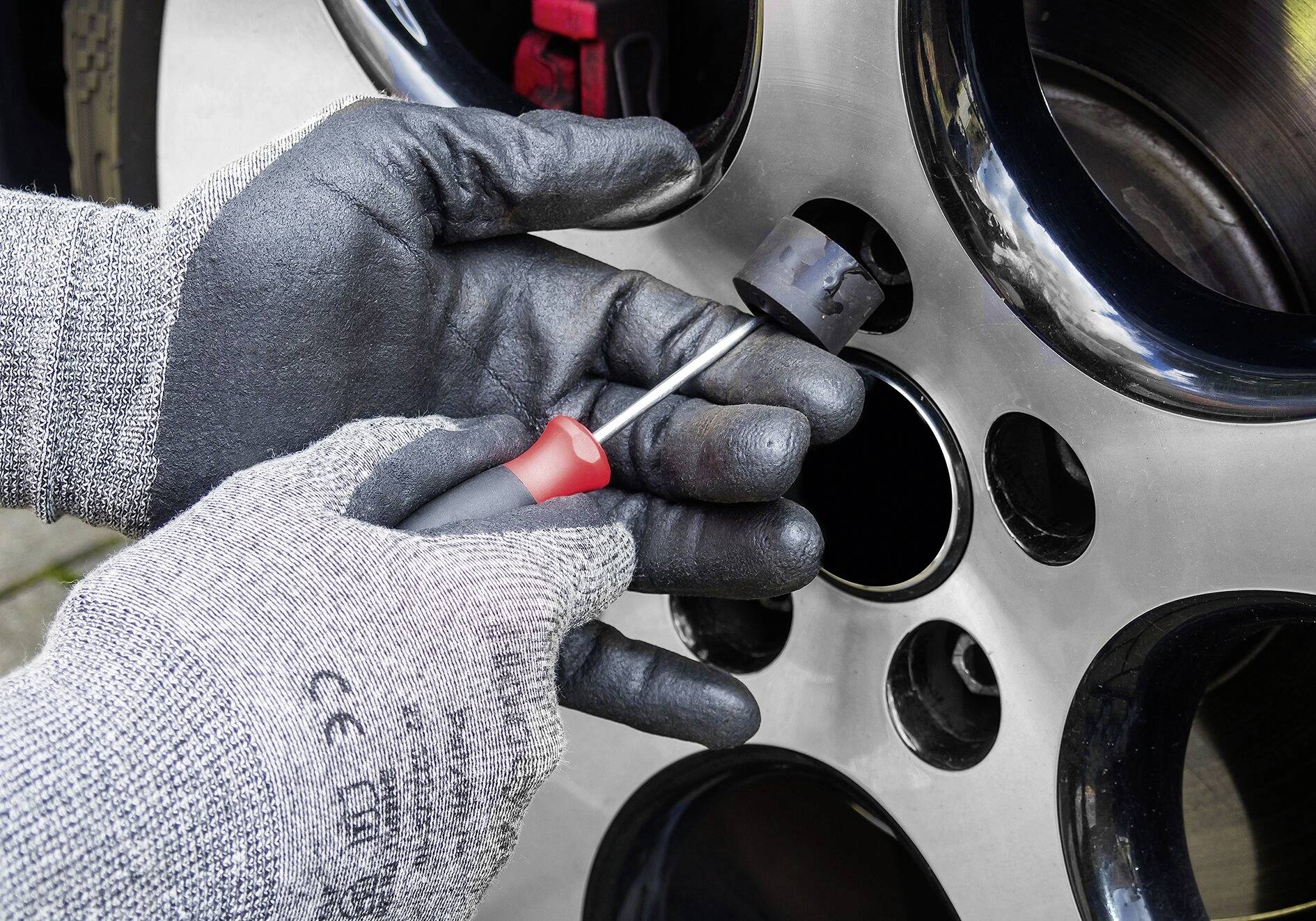 Een persoon monteert een autoband met een schroevendraaier. Handen dragen zwarte, gripvaste handschoenen. Close-up toont wielmoer en velg.