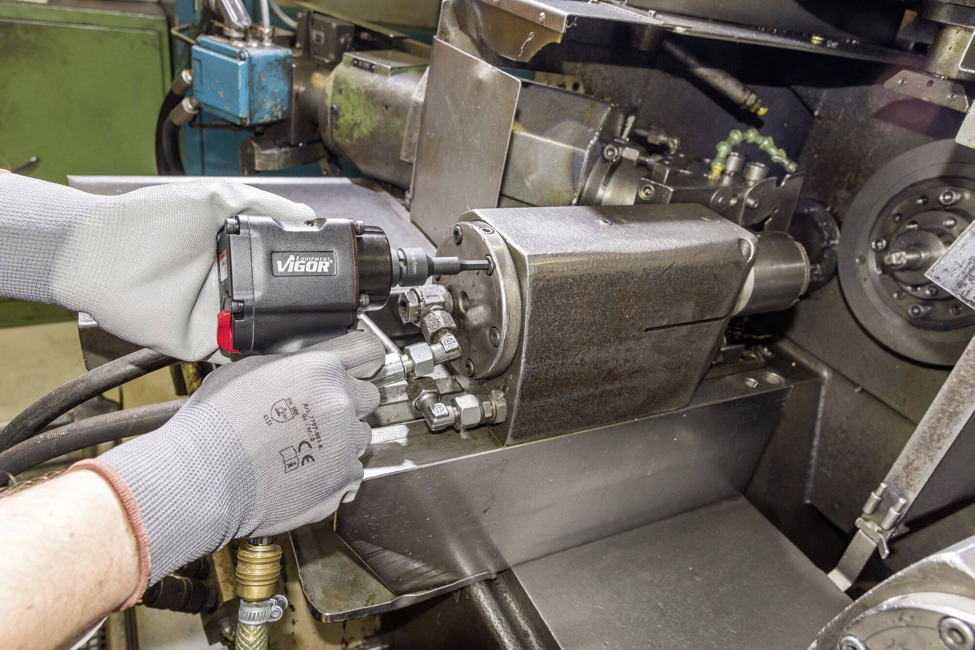 Een persoon met grijze handschoenen gebruikt een pneumatisch gereedschap om een schroef te bevestigen aan een industriële metaalmachine.