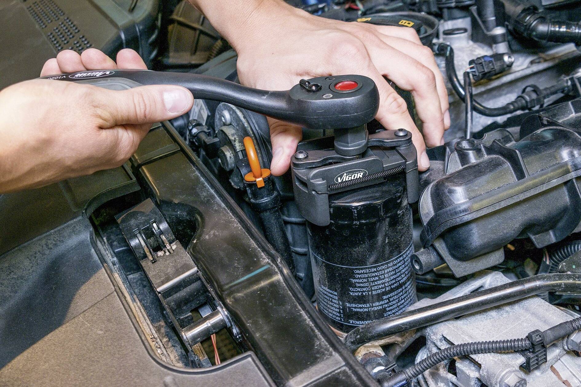 Een persoon repareert een auto-onderdeel met een ratel in de motorruimte. Handen zijn geconcentreerd op een schroef of bevestiging.