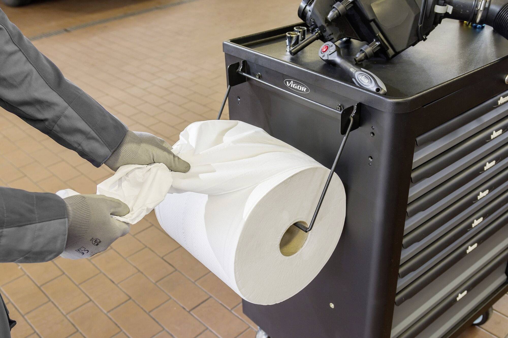 Een persoon trekt een papieren doek van een grote rol die aan een werkplaatswagen is bevestigd. Handschoenen worden gedragen.