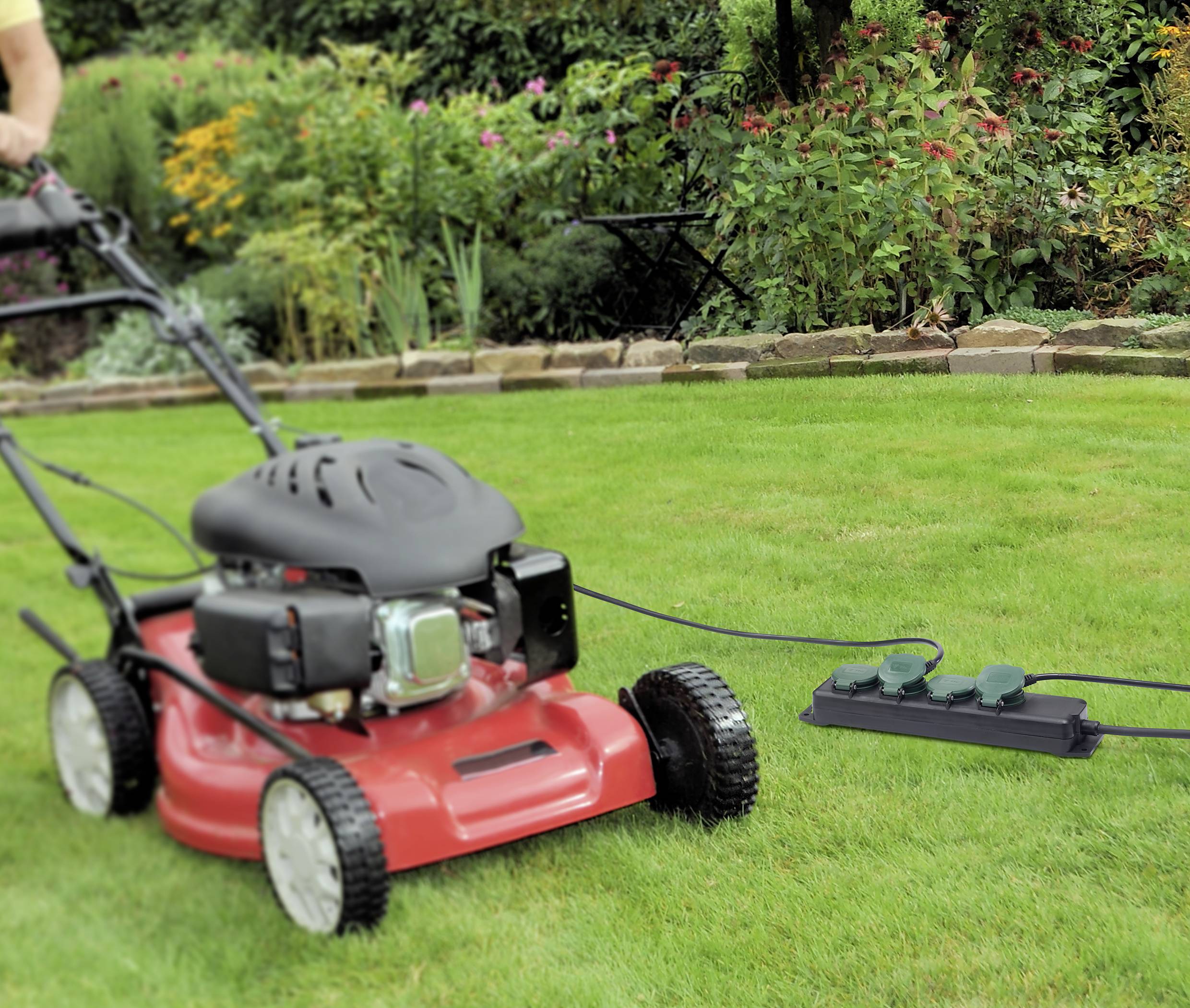 Een grasmaaier wordt gebruikt op een groen gazon in een tuin. De grasmaaier is aangesloten op een verlengkabel.