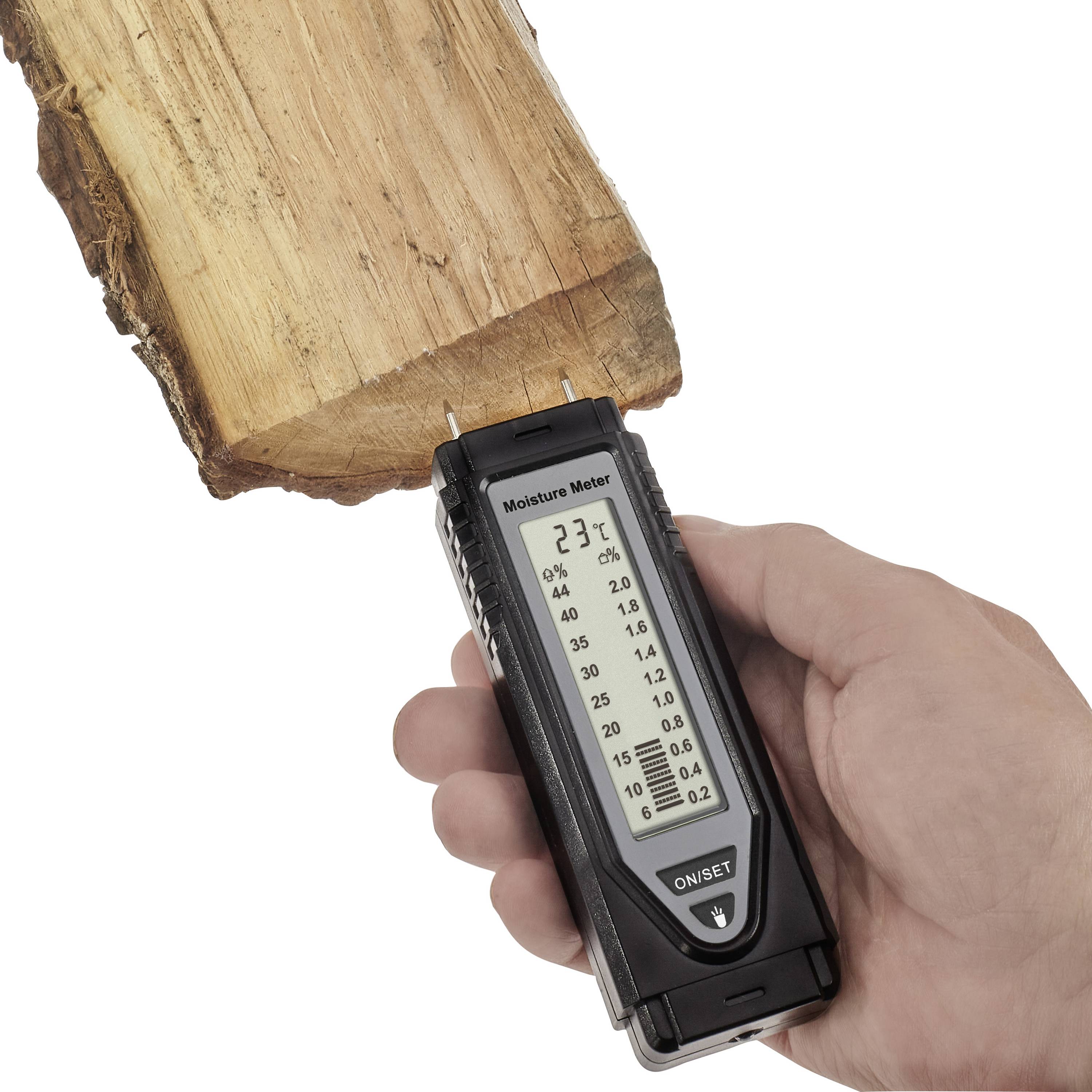 Een hand houdt een vochtigheidsmeter tegen een stuk hout. Het display toont 23% vochtigheid.