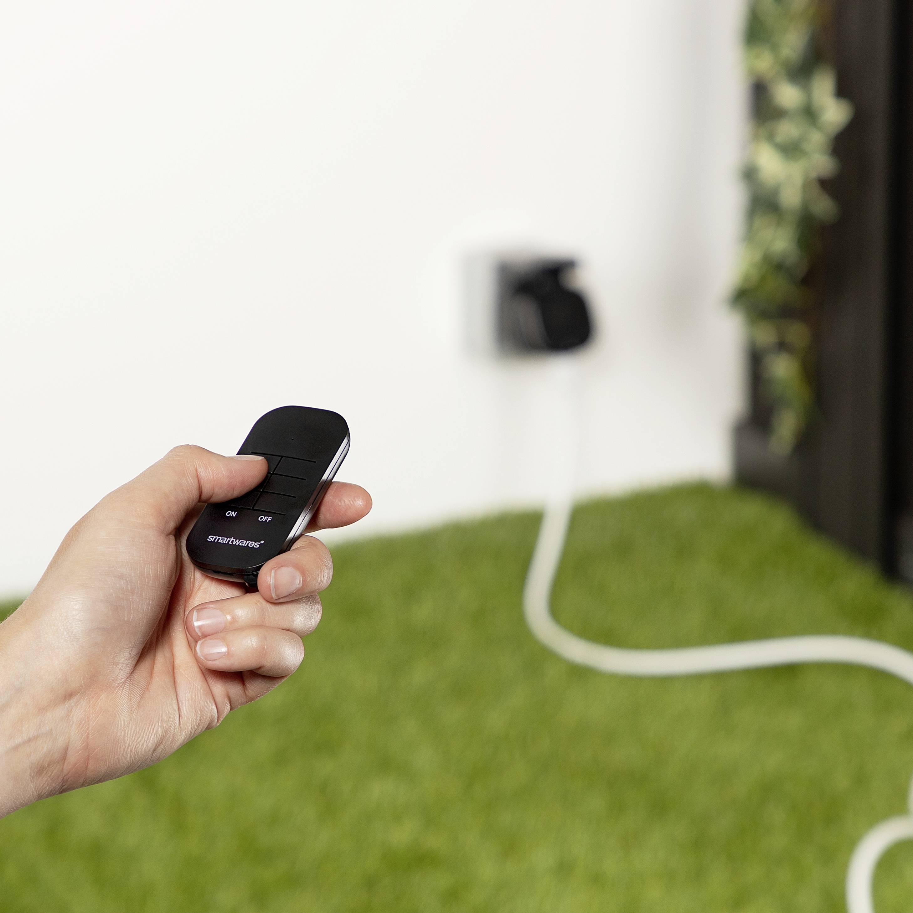 Een hand houdt een afstandsbediening vast in een ruimte met een stopcontact op de achtergrond. Een verlengkabel is zichtbaar.