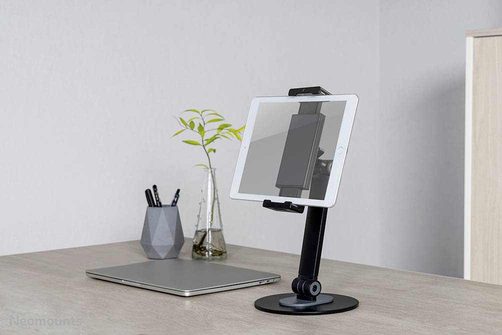 'Bureau met laptop, tablethouder en vaas met plant, moderne en opgeruimde werkplek.'