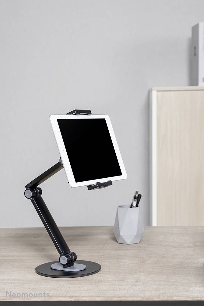 Tablet op een verstelbare armsteun op het bureau; op de achtergrond een pennenhouder en een archiefkast.