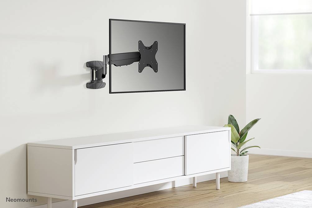 Platte beeldschermsteun aan de muur gemonteerd, kantelbaar en draaibaar, boven een wit dressoir met decoratieve plant rechts.
