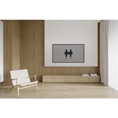 Lichte ruimte met houten vloer, een fauteuil links en een wandsteun voor een tv of monitor aan de witte muur rechts.