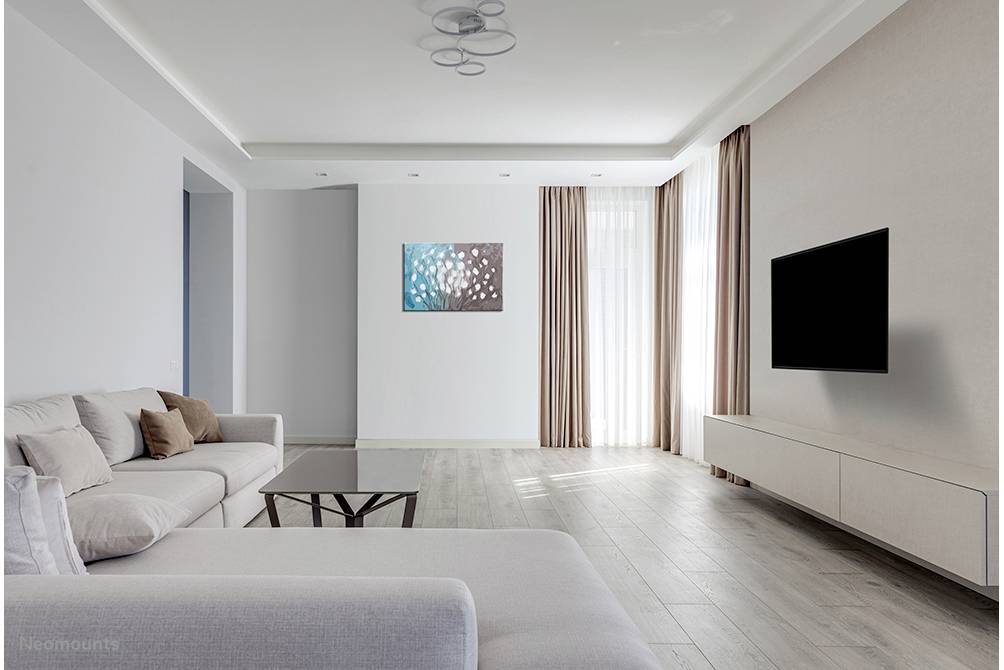 Lichte, minimalistische woonkamer met een grijze bank, een lage tafel en een flatscreen-tv aan de muur.