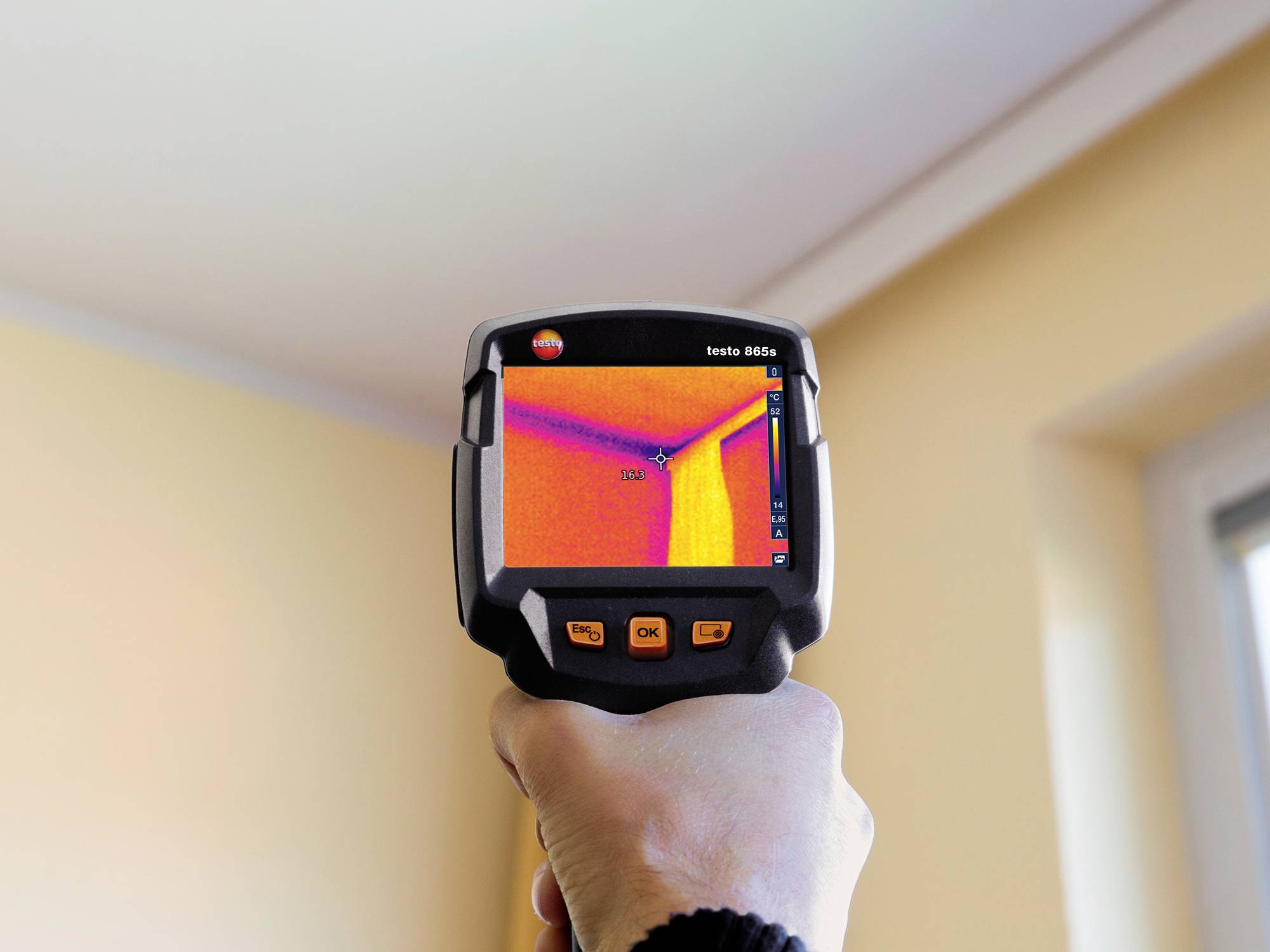 Een hand houdt een thermische camera vast die een muur toont met een duidelijk temperatuurverschil.