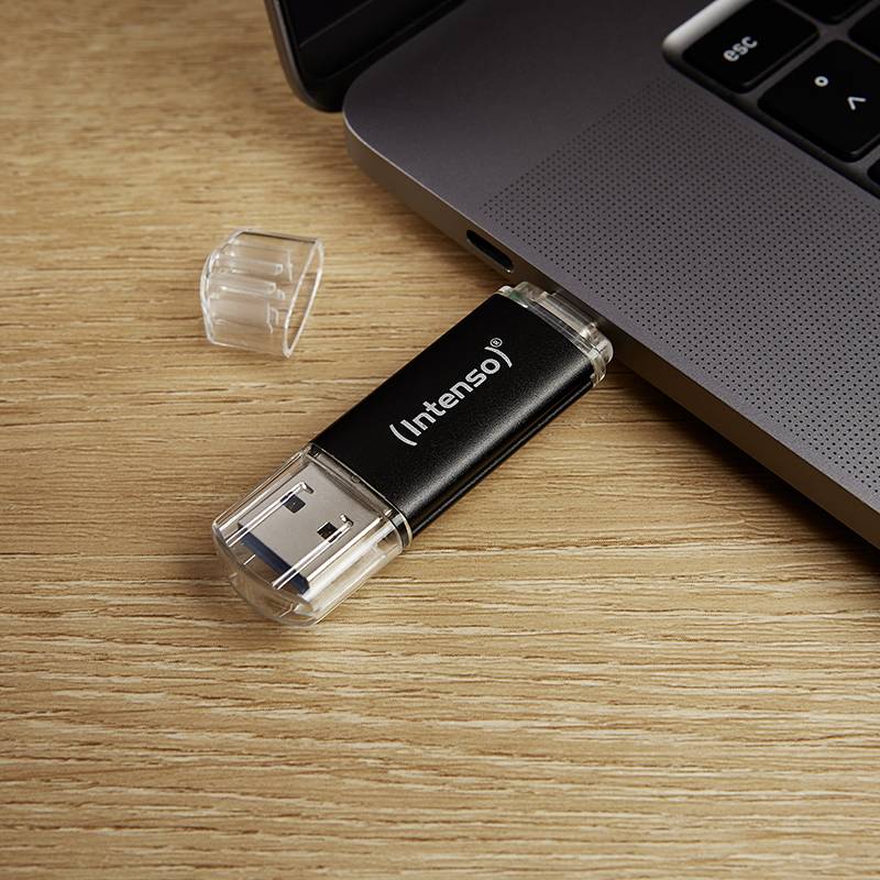 Een zwarte USB-stick van het merk Intenso wordt in een laptop op een houten tafel gestoken.