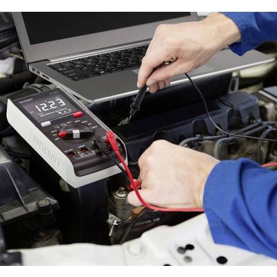 'Een persoon test de autobatterij met een multimeter, terwijl naast hem een laptop geopend is.'