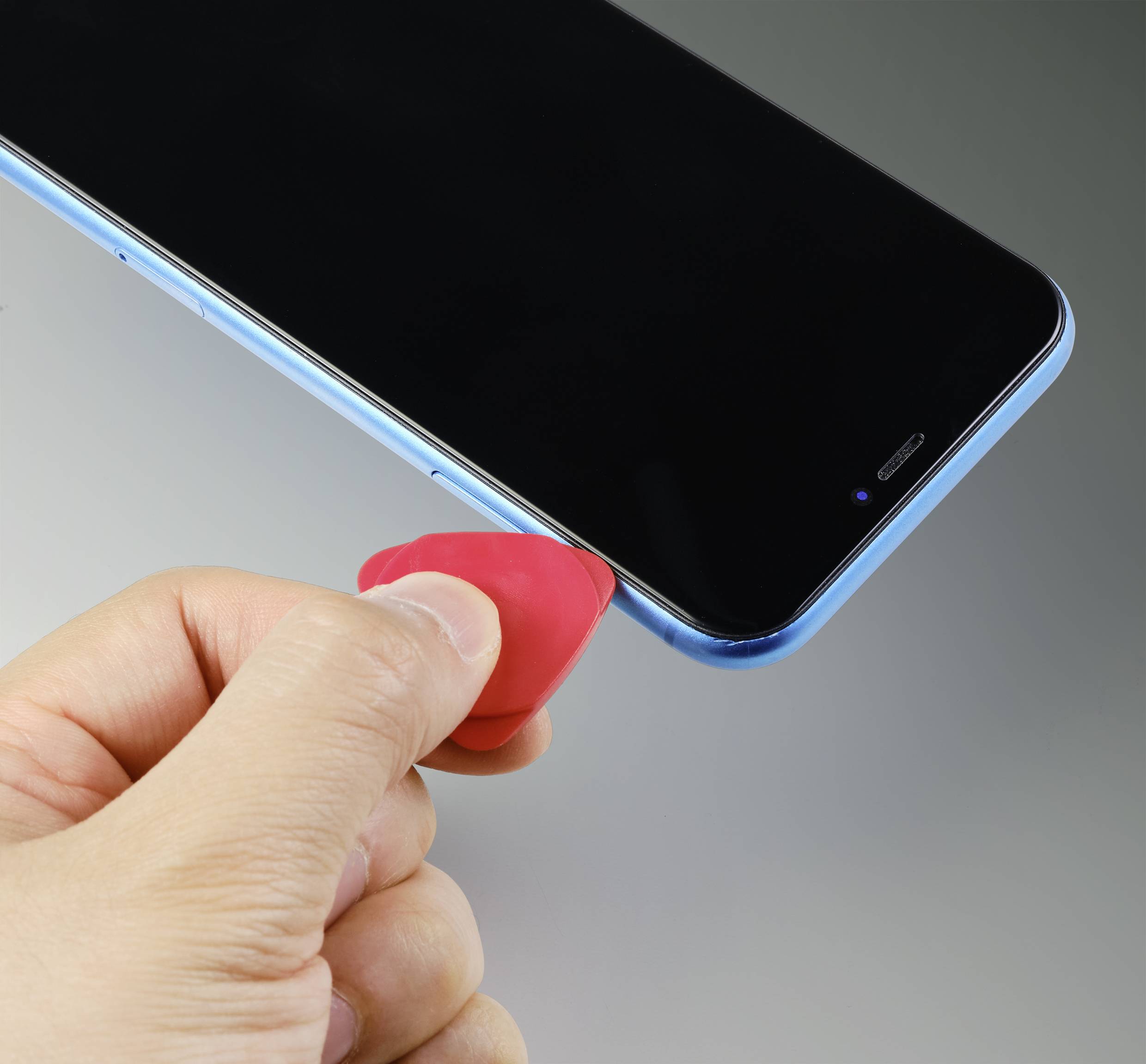Een hand houdt een rode plectrum en verwijdert voorzichtig het scherm van een smartphone voor reparatie of onderzoek.