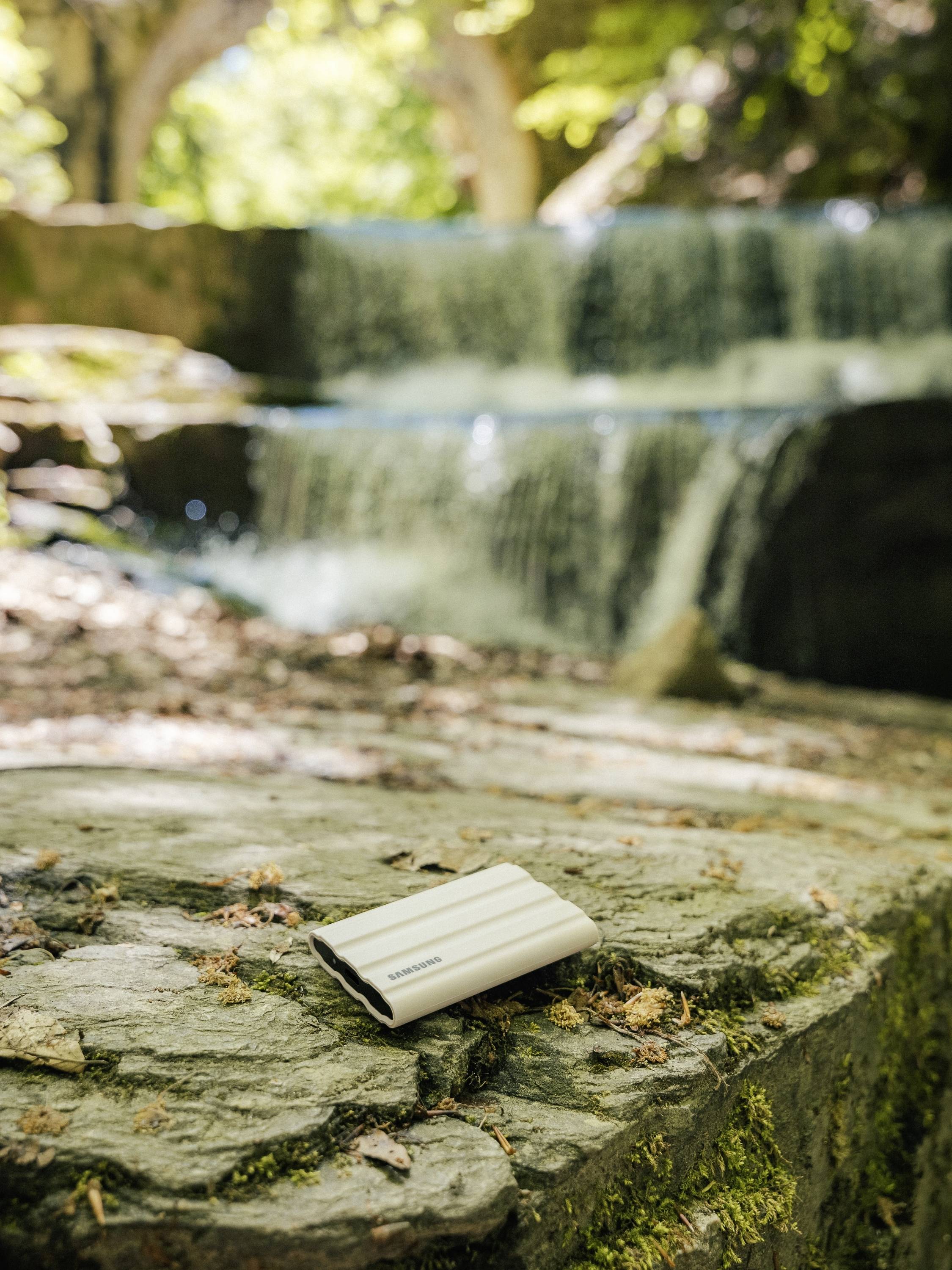 Een klein wit notitieboekje ligt op een rots op de voorgrond, op de achtergrond is een natuurlijke waterval in het bos te zien.