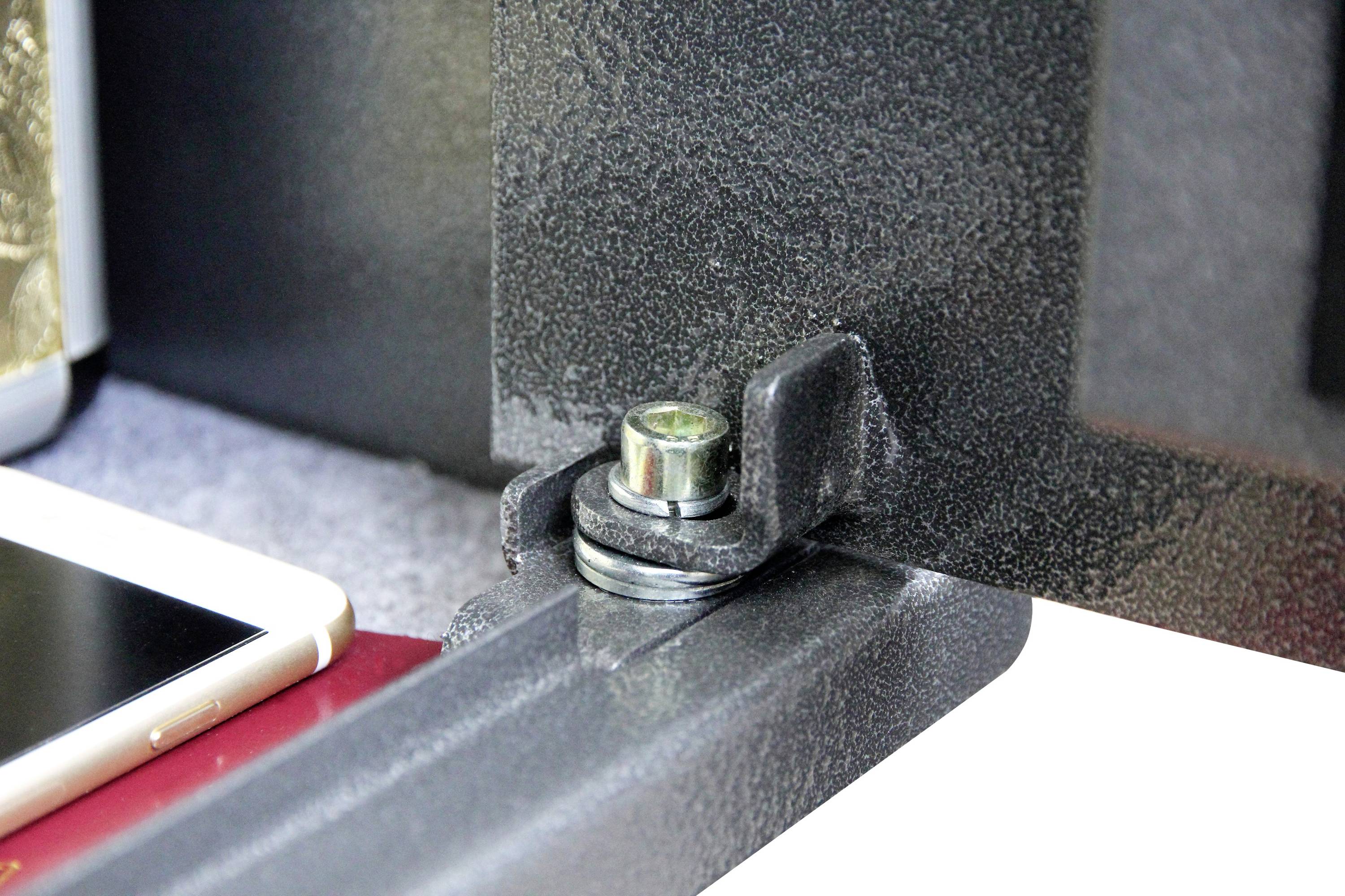 Close-up van een metalen scharnier op een kluis. Een smartphone en een rood document zijn in de buurt zichtbaar.