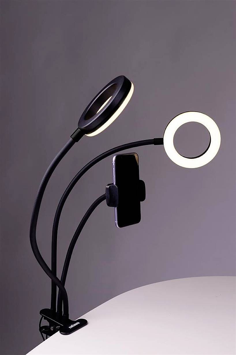 Een dubbel-armige ringlamp met een telefoonhouder, gemonteerd op een tafel. Ideaal voor video-opnames met gelijkmatige verlichting.
