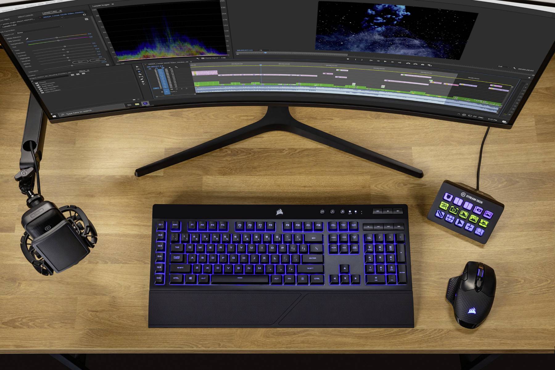 Een bureau met een gebogen monitor die een videobewerking programma weergeeft. Een toetsenbord met blauwe toetsen licht op.