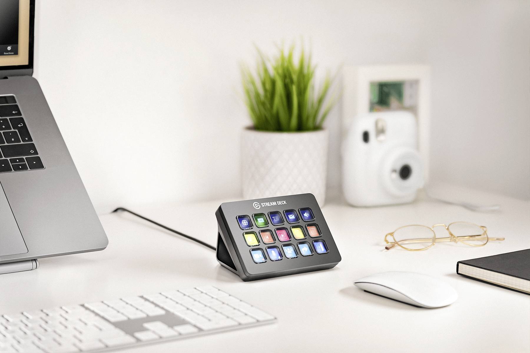 Een werkruimte met een laptop, een toetsenbord, een muis, een brillenkoker, een plant, een camera en een Stream Deck.