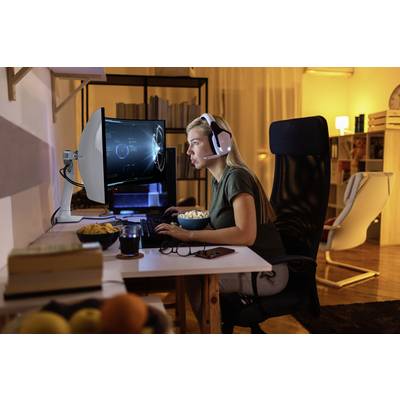 Een persoon zit aan een computer en draagt een headset. Op het scherm zijn futuristische grafische weergaven. De omgeving oogt gezellig.