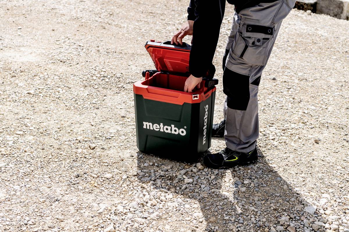 Een persoon opent een Metabo-gereedschapskist buiten op een grindvloer.