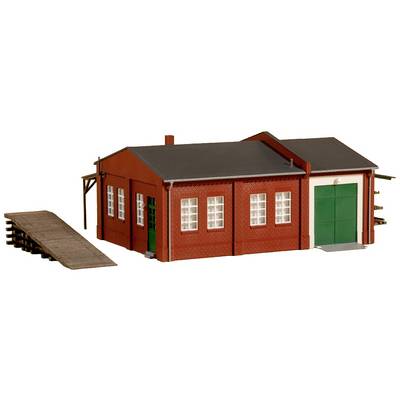 Een rood bakstenen gebouw met een groen hek en meerdere ramen. Een houten oprit leidt naar het gebouw. Model van een pakhuis.
