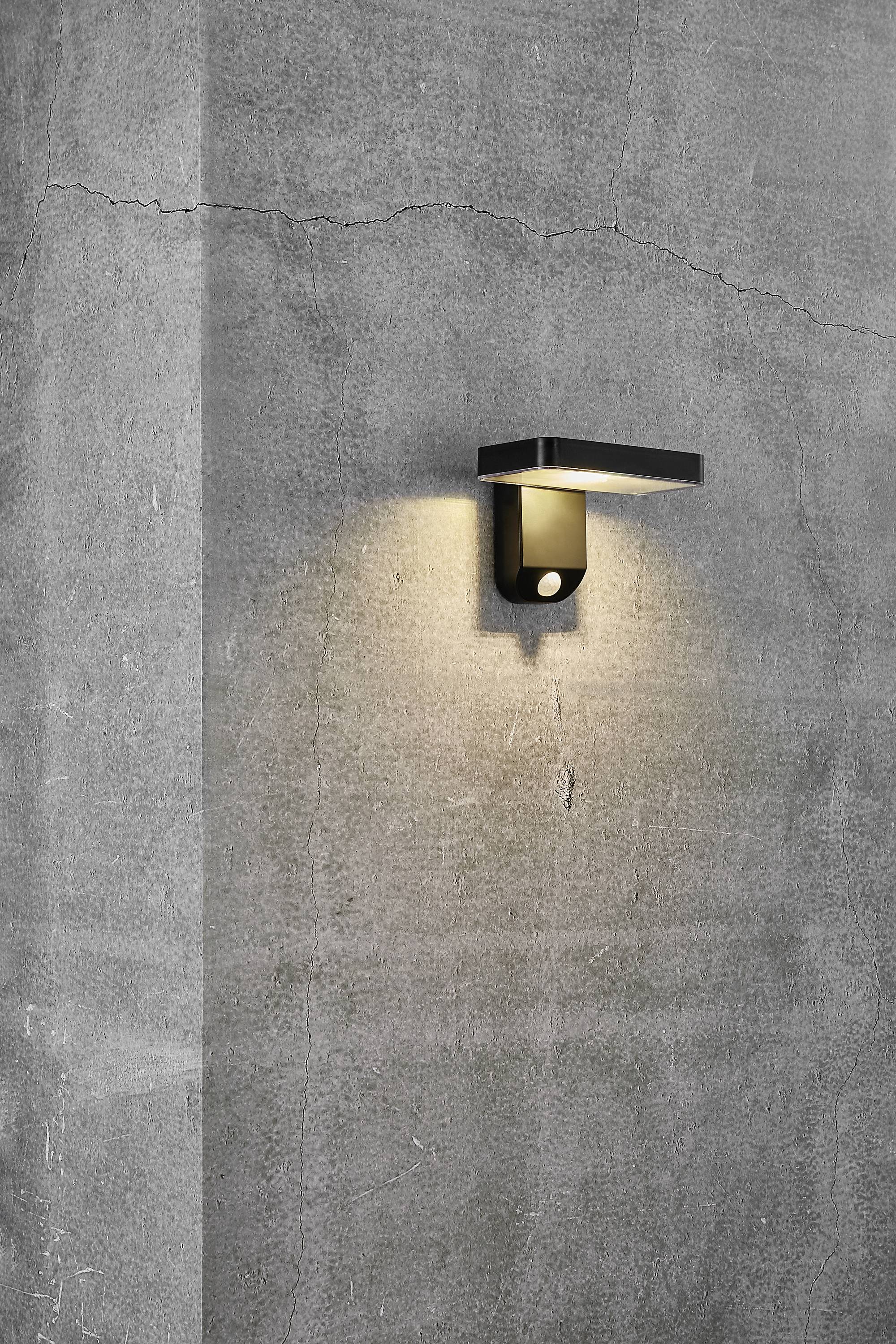 Buitenlamp met een eenvoudige, moderne vormgeving verlicht een grijze betonnen muur en creëert een warme lichtgloed.